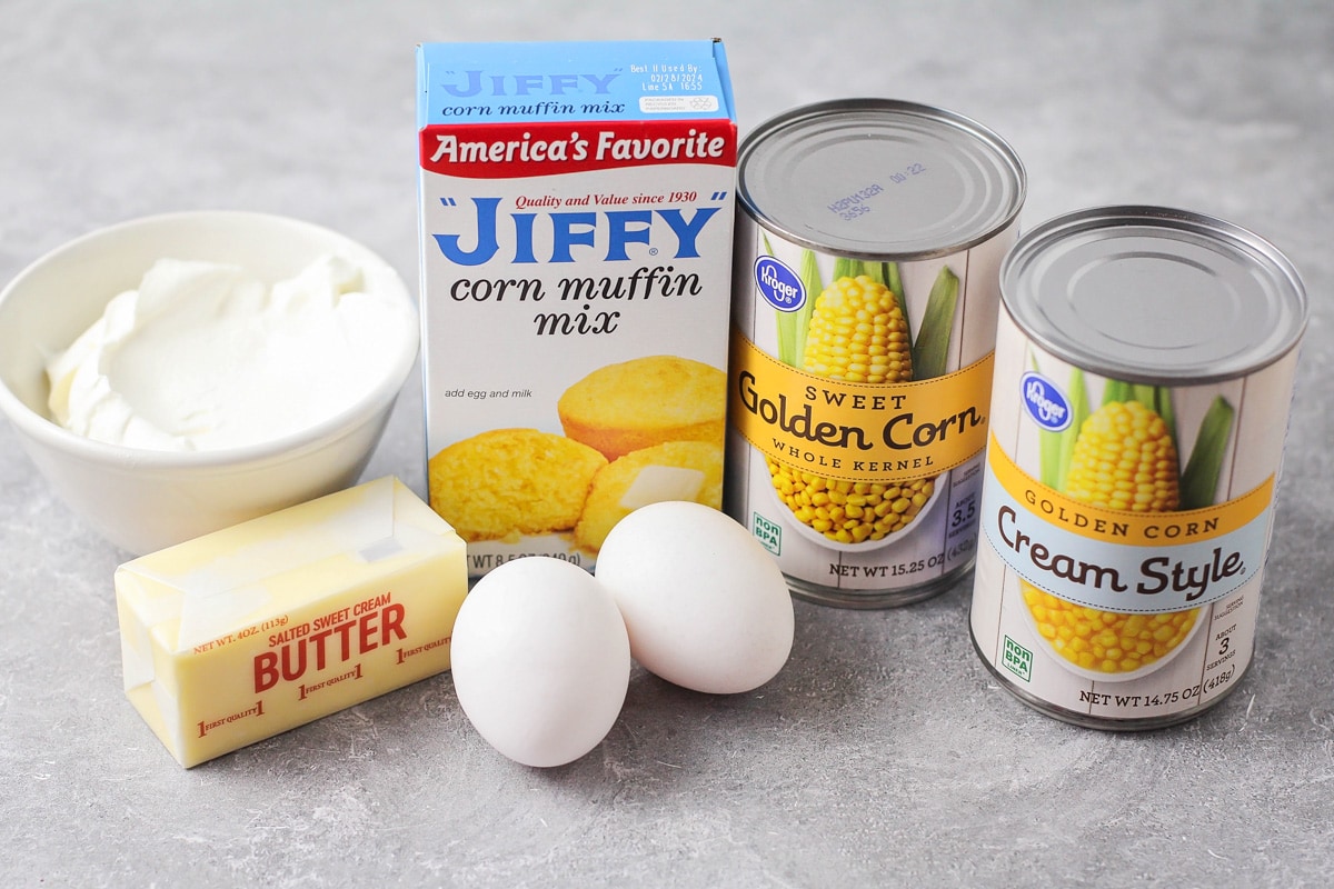 Jiffy mix, canned corn, buttter, eggs, and sour cream set out on a kitchen counter.