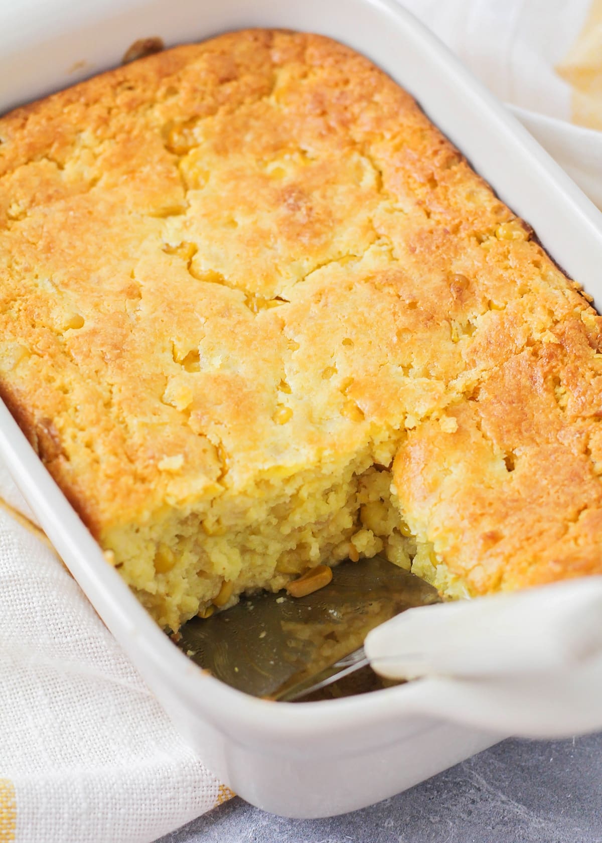 A slice of corn casserole missing from a white baking dish.