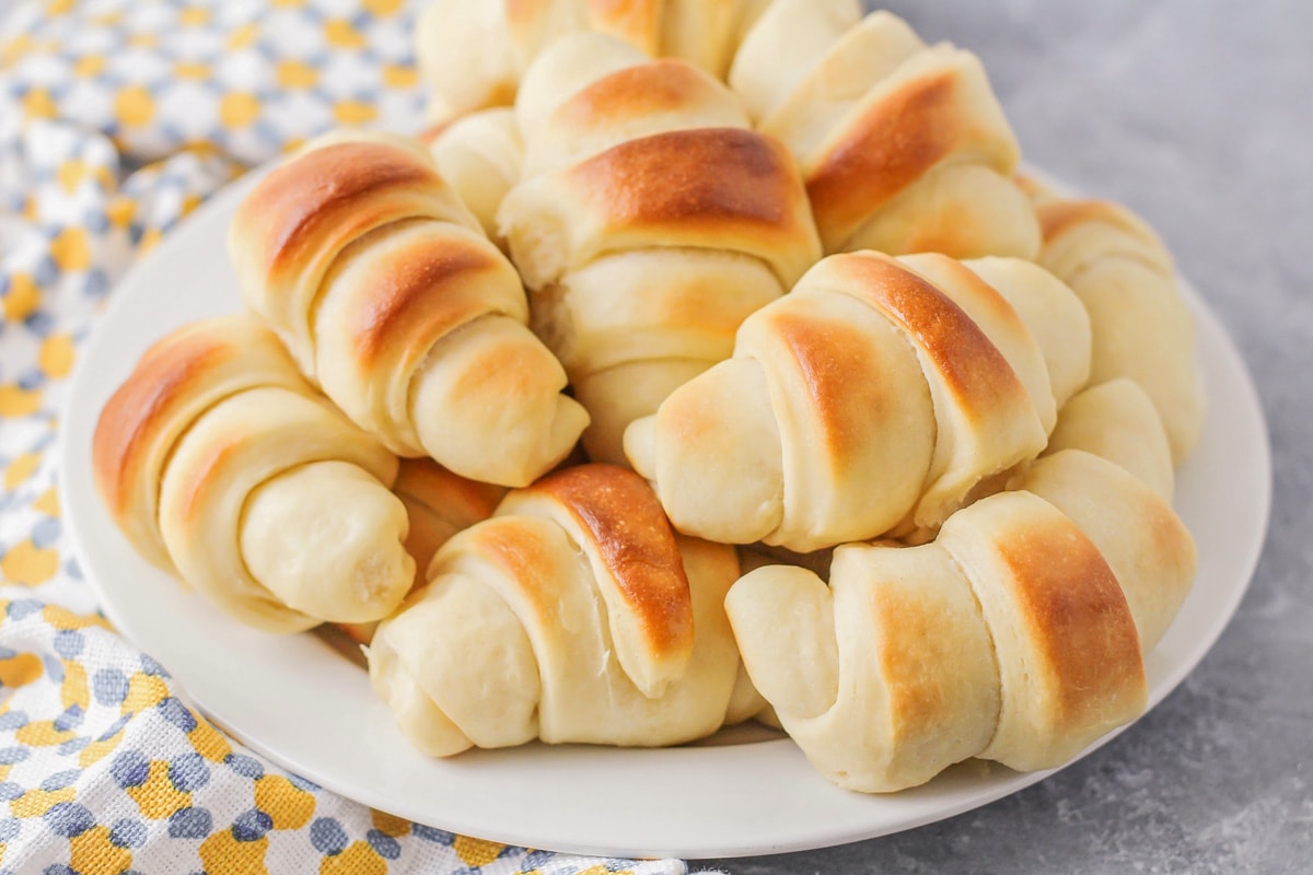 Homemade dinner rolls piled on a white plate.