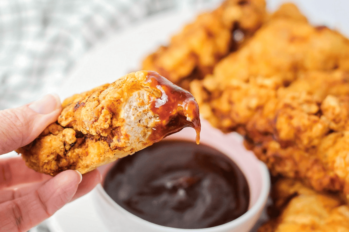 Chicken fingers being dipped in bbq sauce.