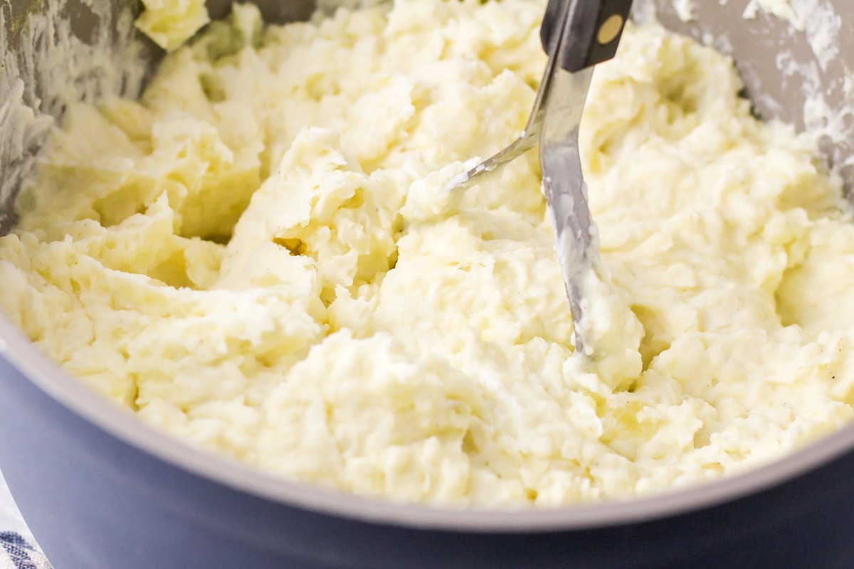 Mashing potatoes with cream cheese and sour cream.