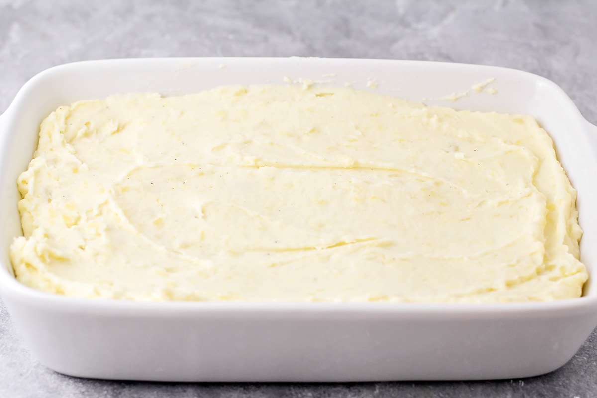 Spreading seasoned mashed potatoes in a white baking dish.