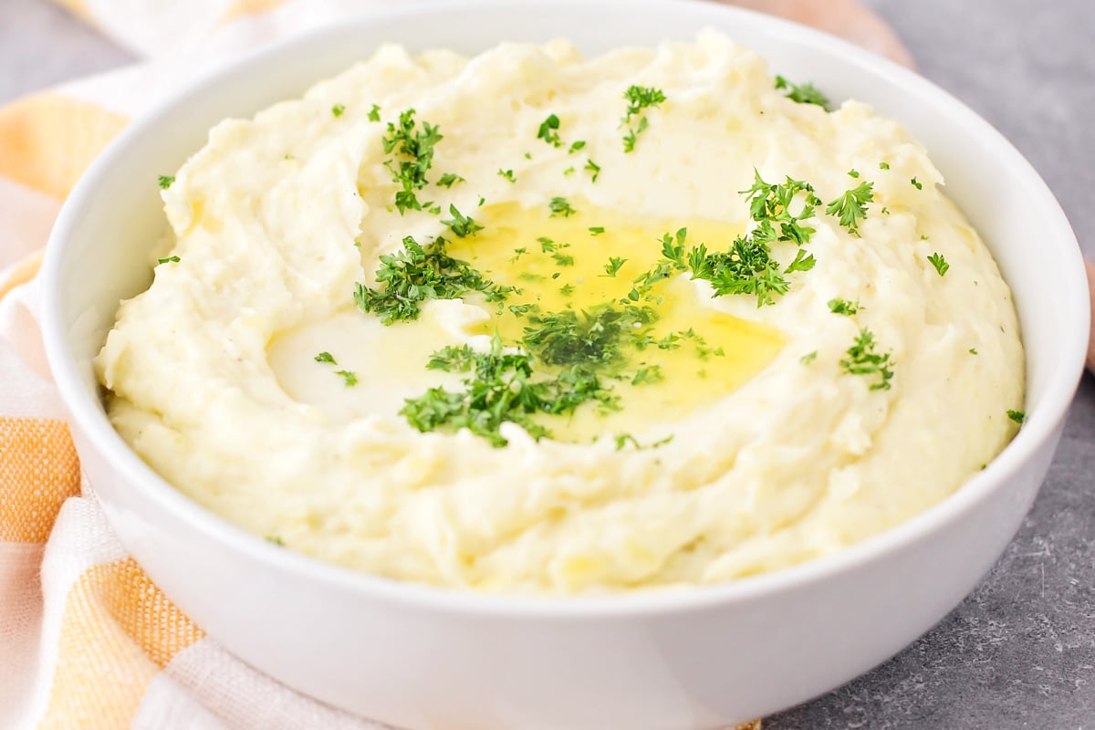 A bowl filled with make ahead mashed potatoes topped with fresh herbs and melted butter.