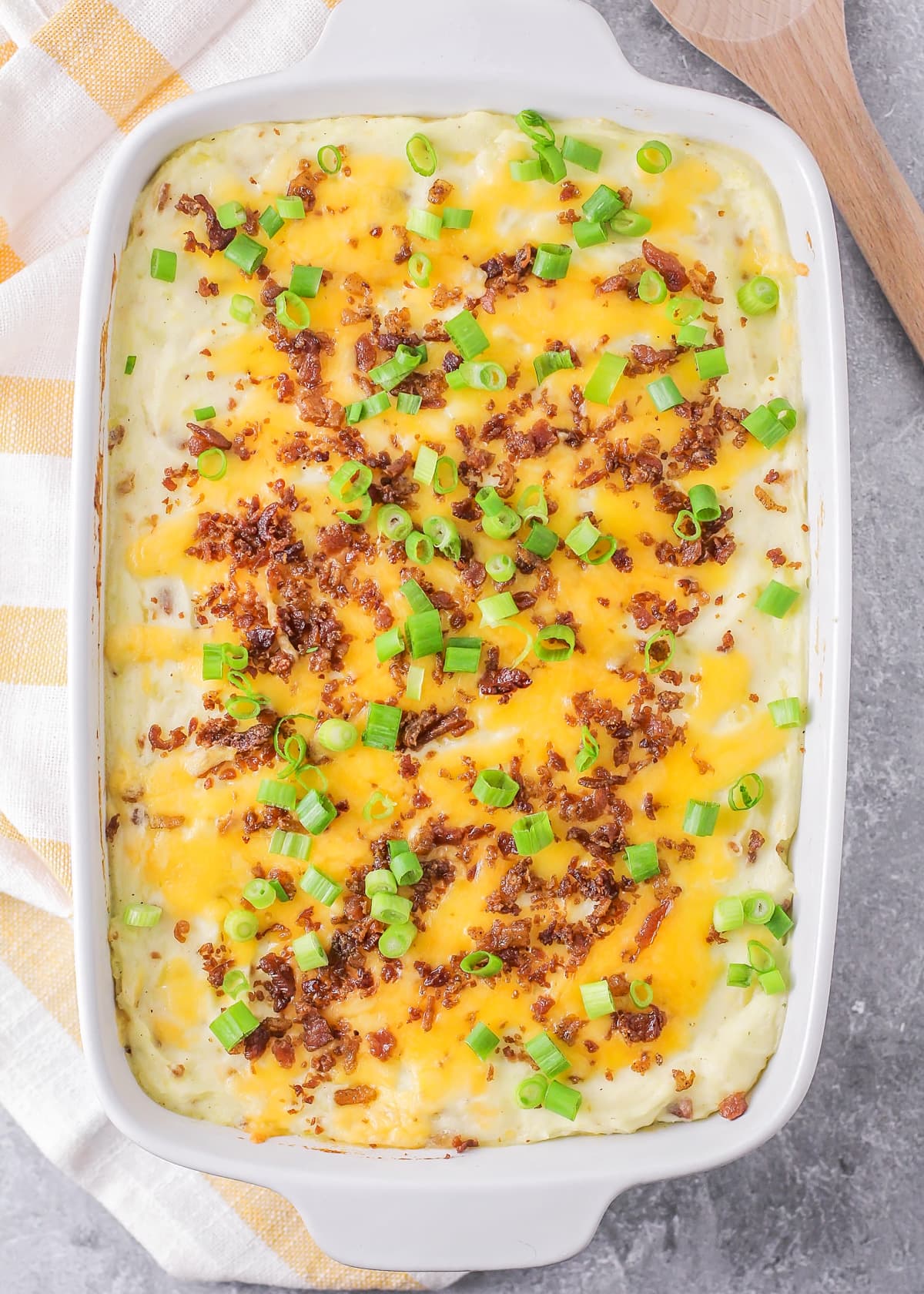 Close up of mashed potato casserole topped with cheese, green onions, and bacon.