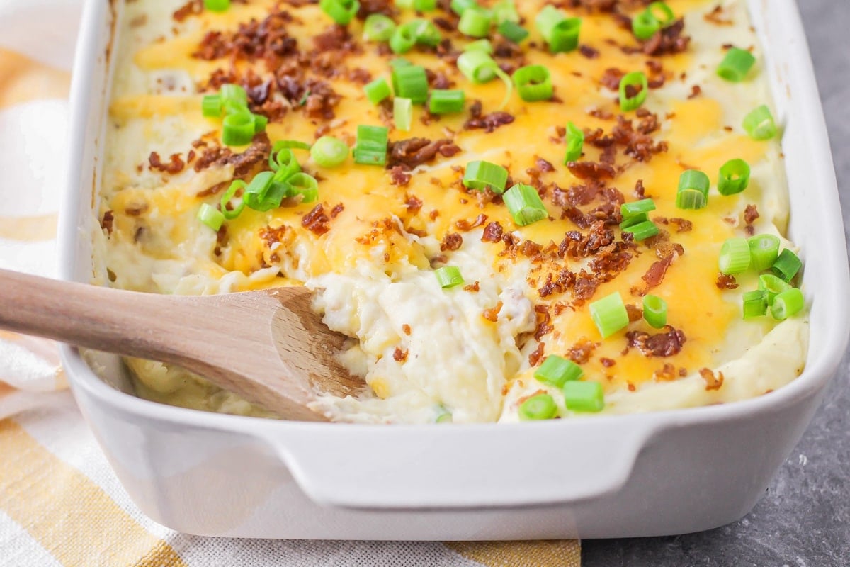 Close up of a casserole dish of loaded mashed potato casserole topped with cheese, bacon, and green onions.