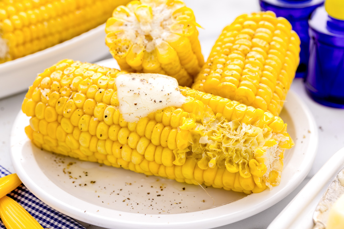 Microwave corn on the cob stacked on  a plate, seasoned with butter and pepper.