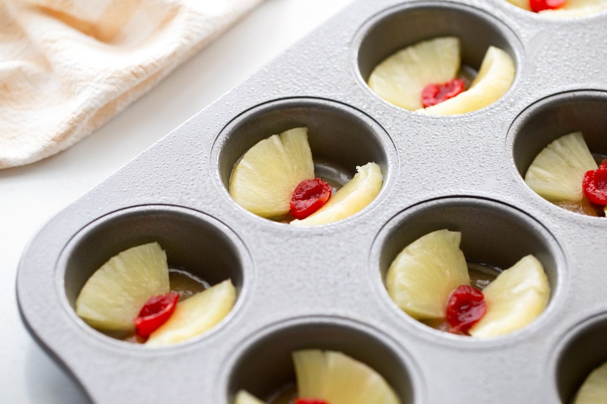 Putting pineapple and cherries in the bottom of a cupcake tin.