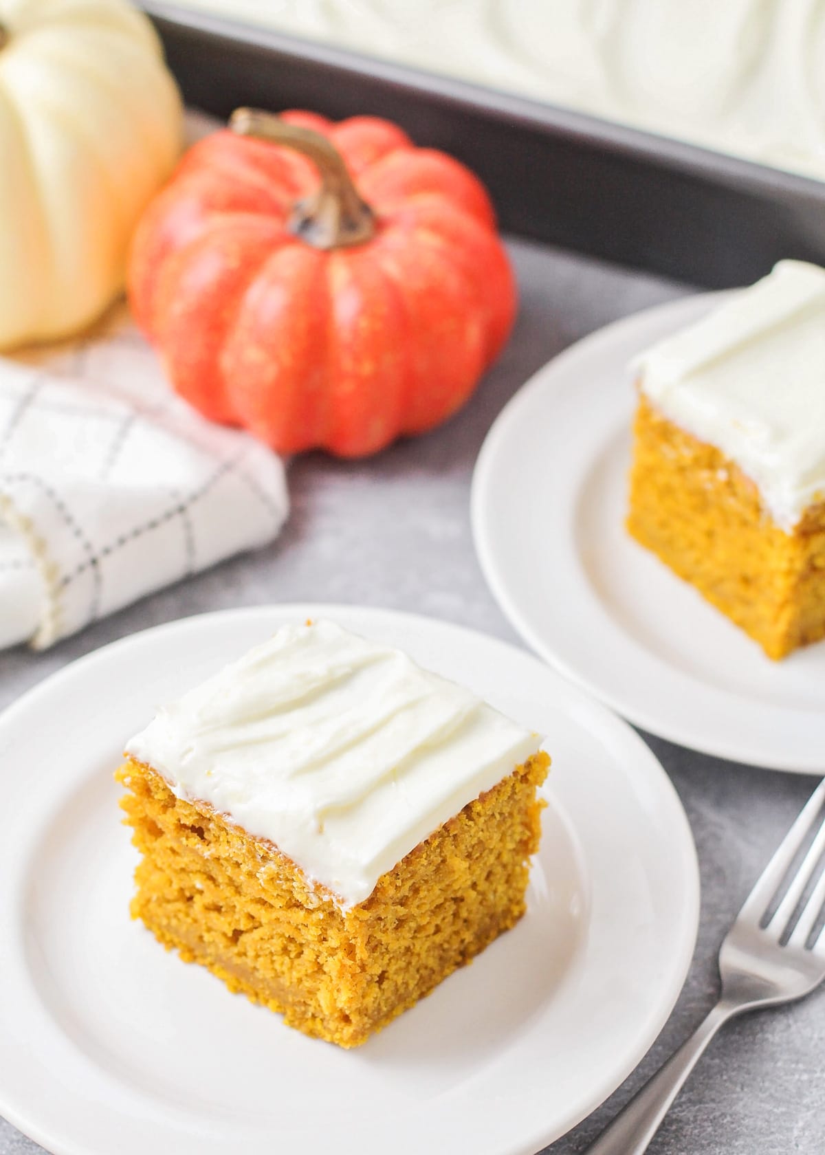 Recipe for pumpkin cake with cream cheese frosting sliced and on a white plate.