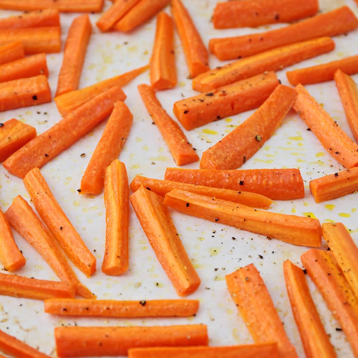 Carrots sticks coated with olive oil and seasoning, spread on a baking sheet.