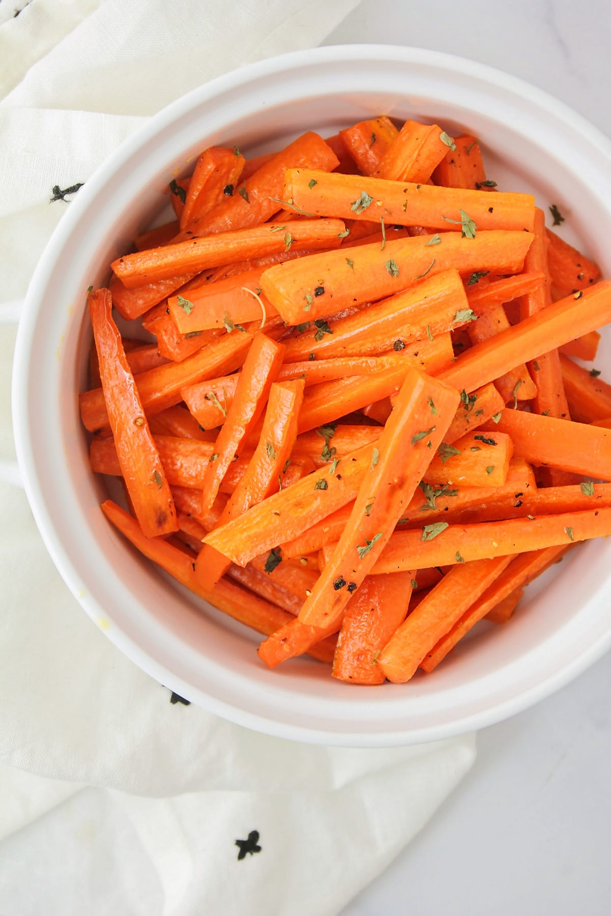 Close up of a bowl filled with roasted carrots topped with dried herbs.