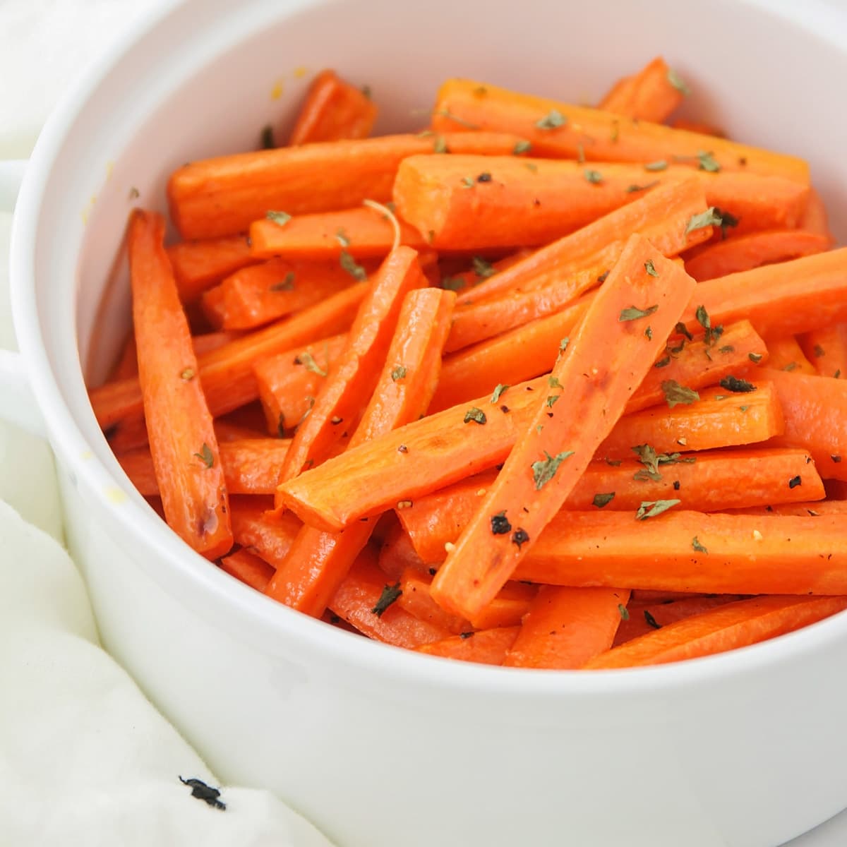 A white bowl filled with roasted carrots sprinkled with dried herbs.