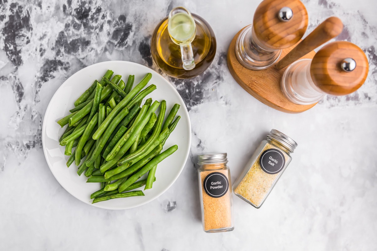 Fresh green beans and seasonings on a countertop.
