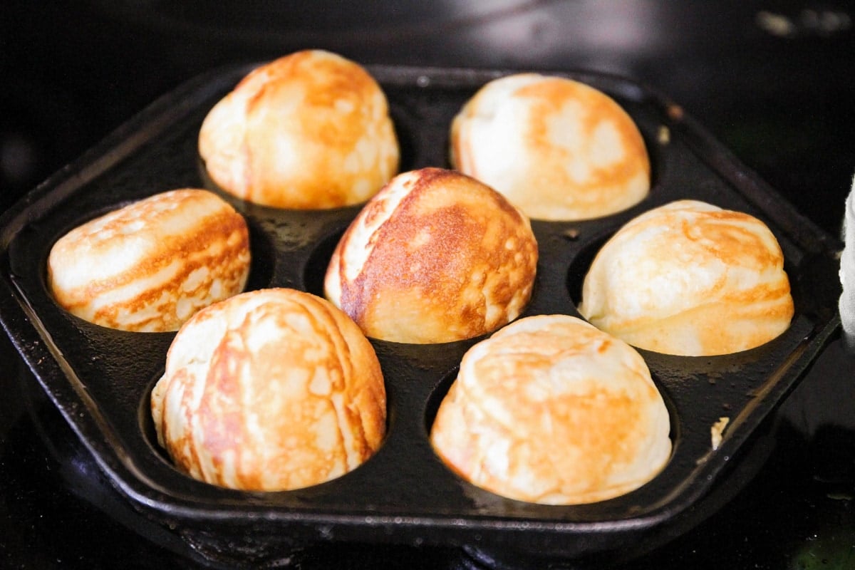 Danish pastry balls cooking in a cast iron pan.