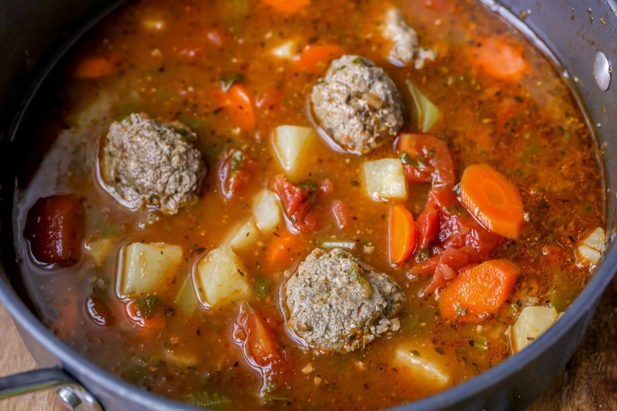 Veggies and meatballs in a broth cooking in a pot.