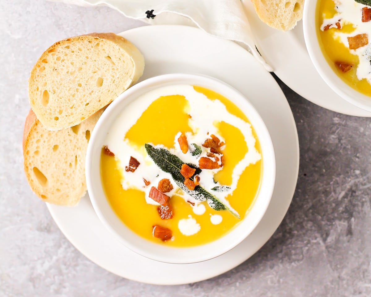 A bowl filled with butternut squash soup and topped with cream and prosciutto.