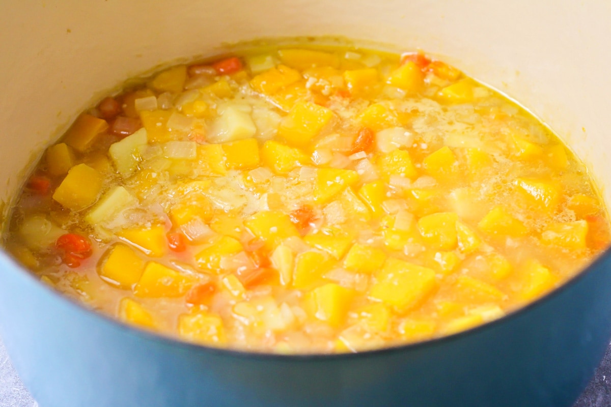 Veggies and cubed squash cooking in liquid in a dutch oven.