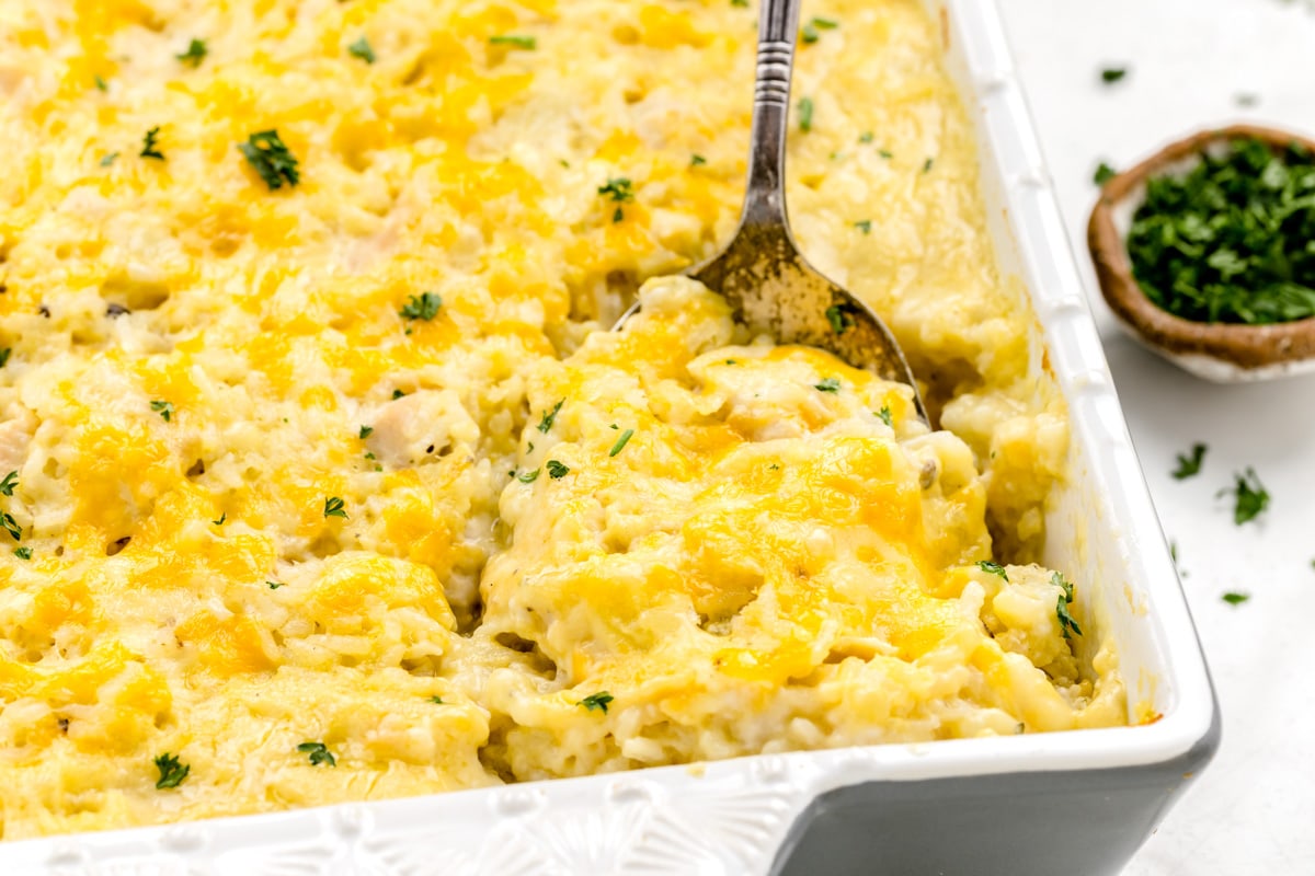 Baked chicken and rice casserole in white casserole dish and a serving spoon.
