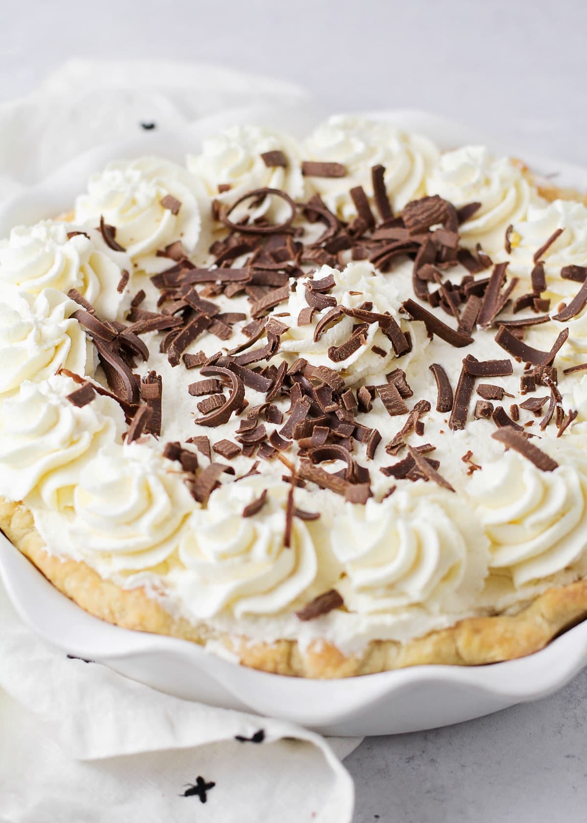 A close up of a chocolate cream pie recipe topped with whipped cream and chocolate curls.