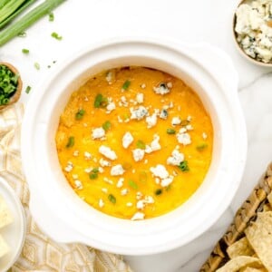 Crock pot buffalo chicken dip topped with fresh sliced scallions and served with tortilla chips.