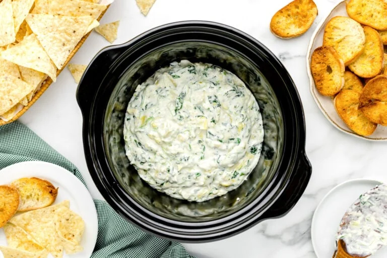 Crockpot Spinach Artichoke Dip in slow cooker with dippers all around.