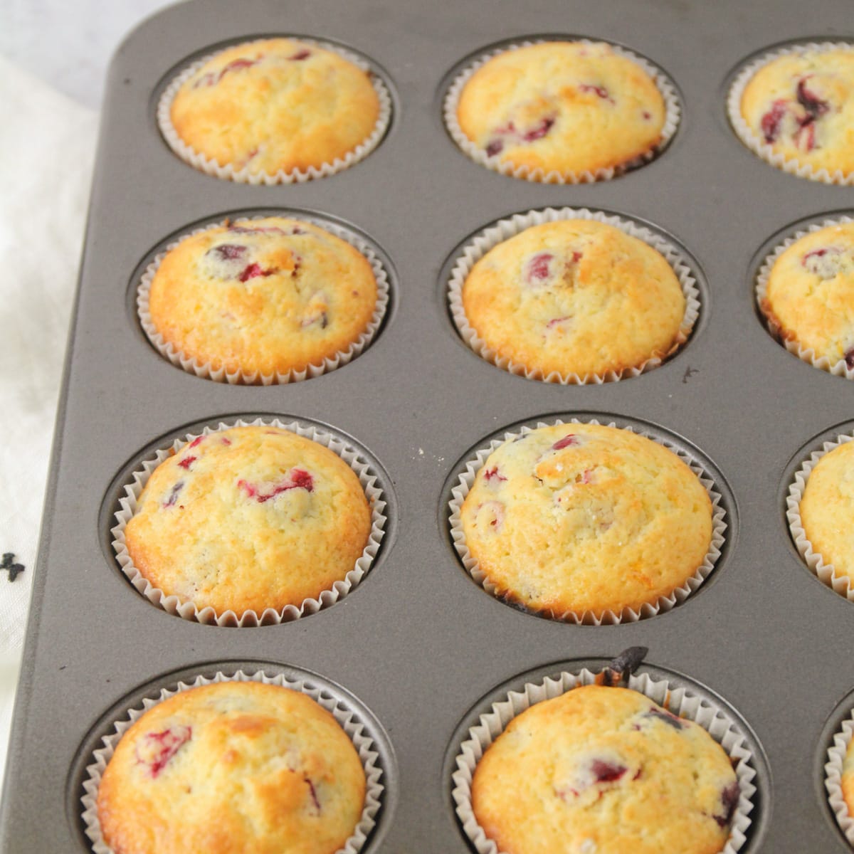 Baked muffins filled with cranberries and orange pieces in a tin.
