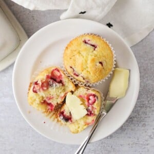 Cranberry Orange Muffins on a plate cut in half one with butter.