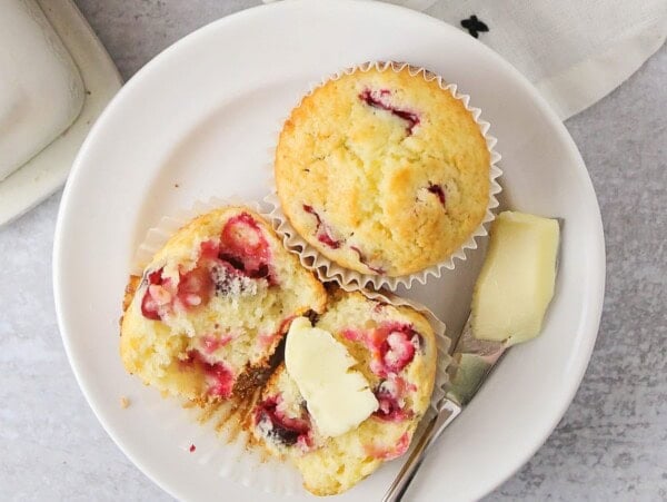 Cranberry Orange Muffins on a plate cut in half one with butter.