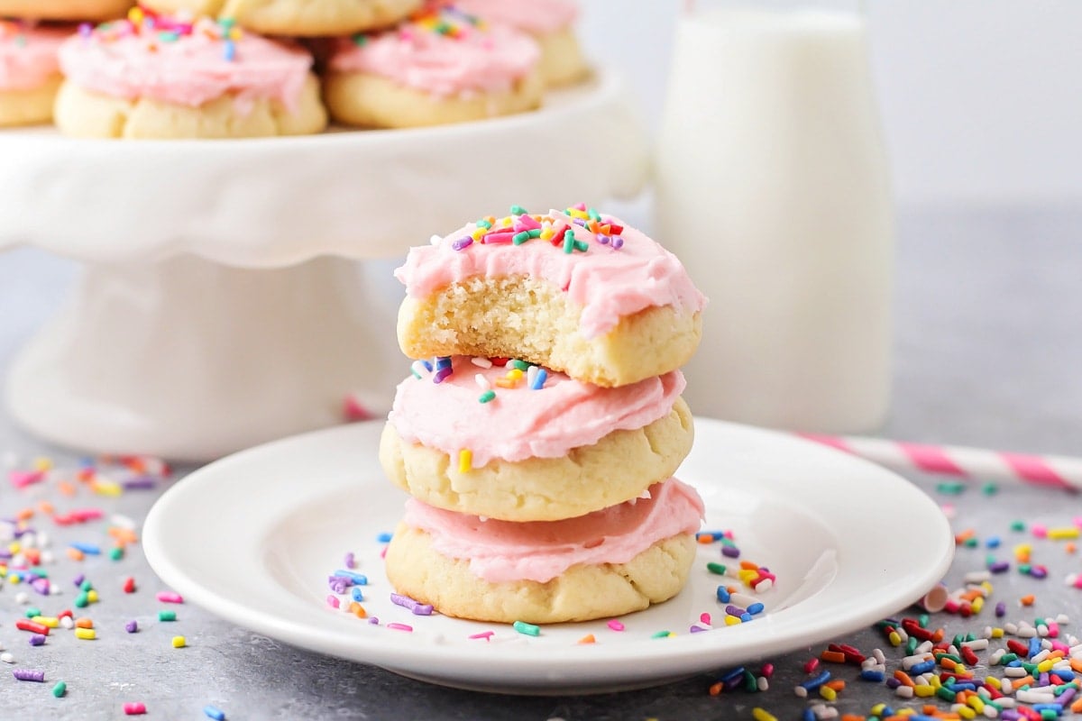 A stack of pink frosted drop sugar cookies on a white plate.