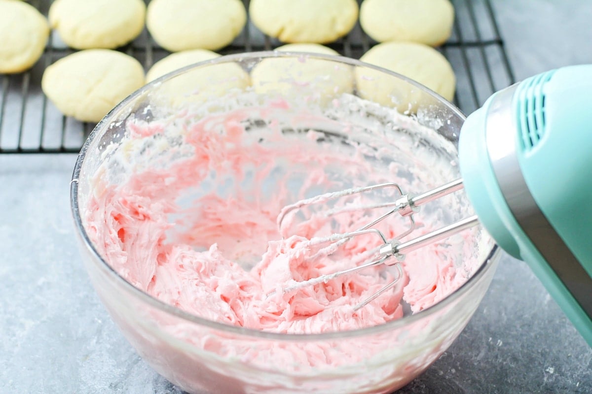 Whipping pink frosting in a glass bowl.