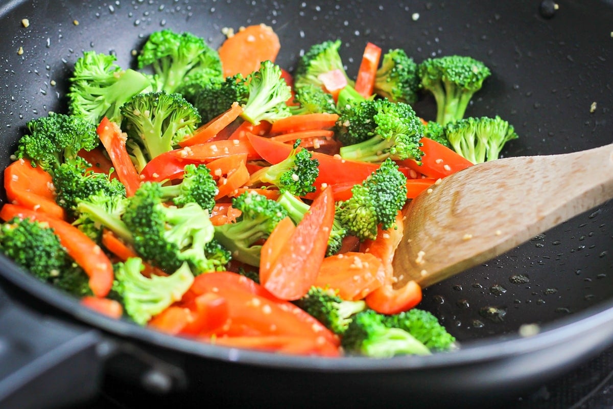Seasoned broccoli, carrots, and peppers cooking in a wok on the stove.