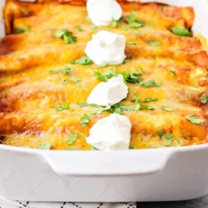 A baking dish filled with ground beef enchiladas, topped with melted cheese and dollops of sour cream.