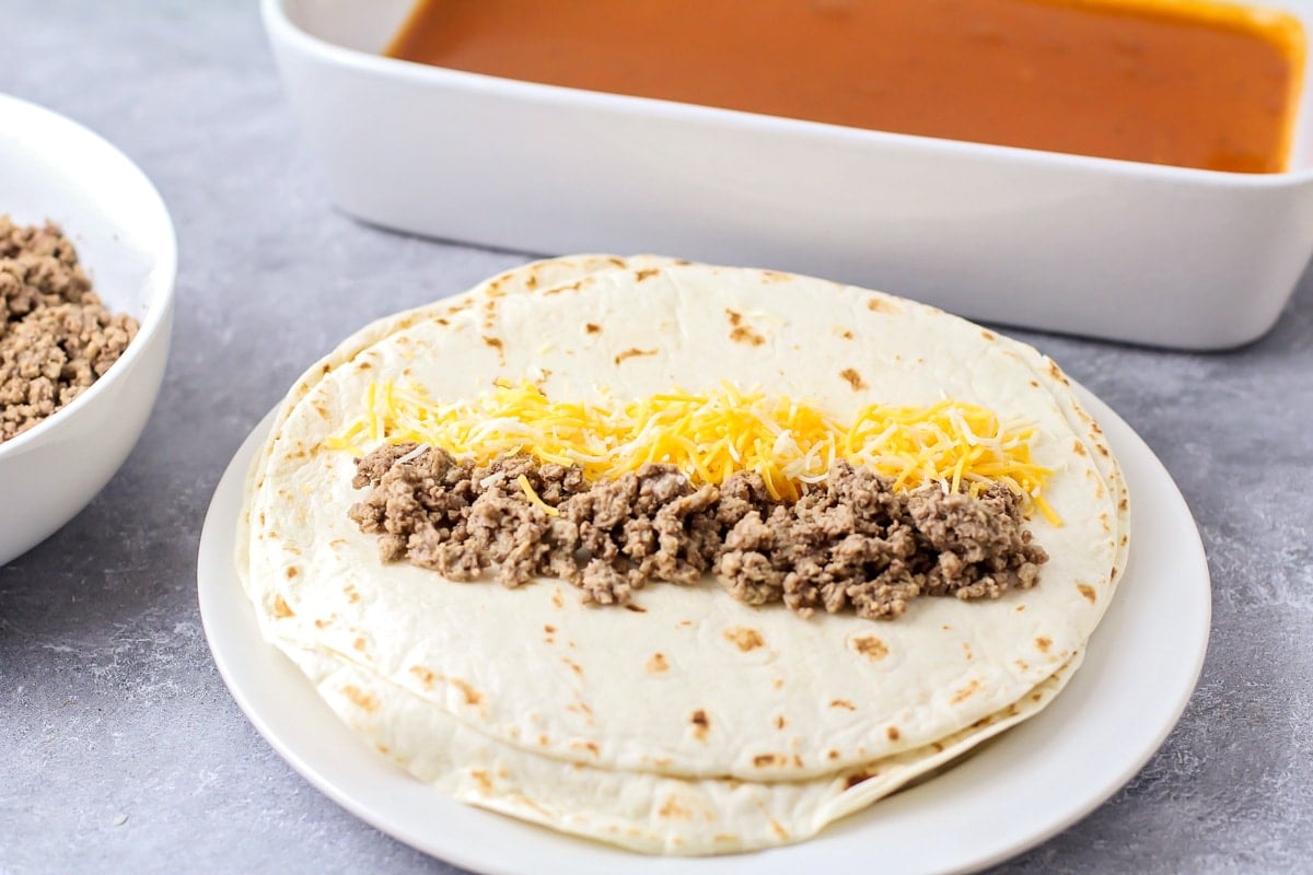 Filling tortillas with ground beef and shredded cheese.