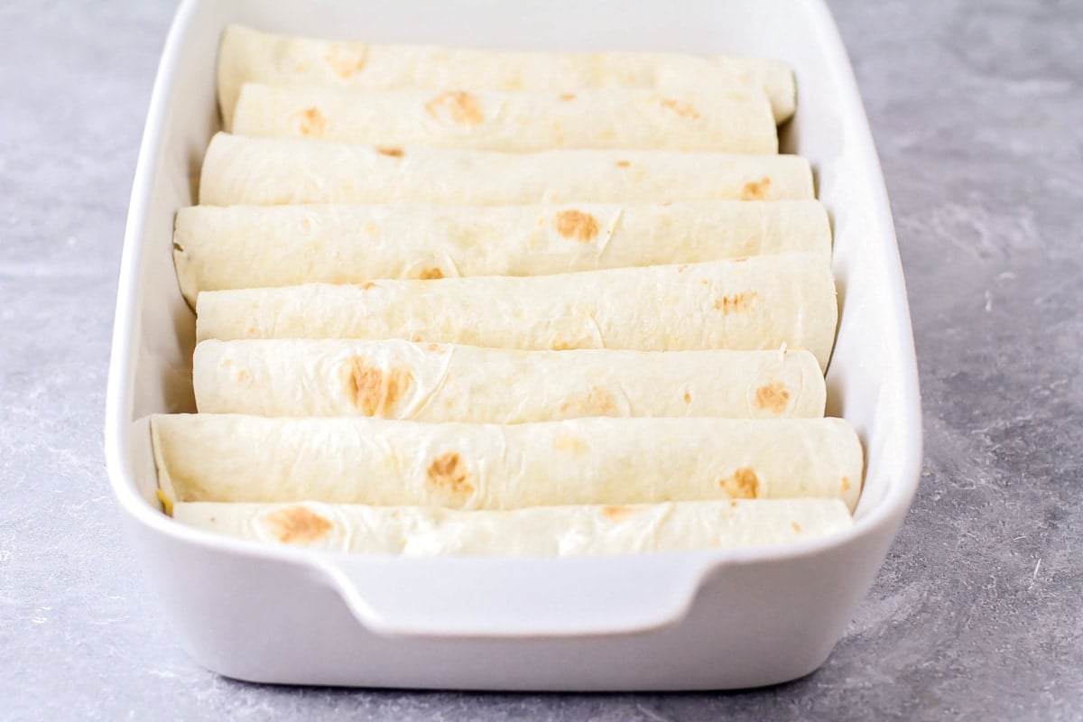 Rolled tortillas filled with ground beef and cheese lined up in a baking dish.