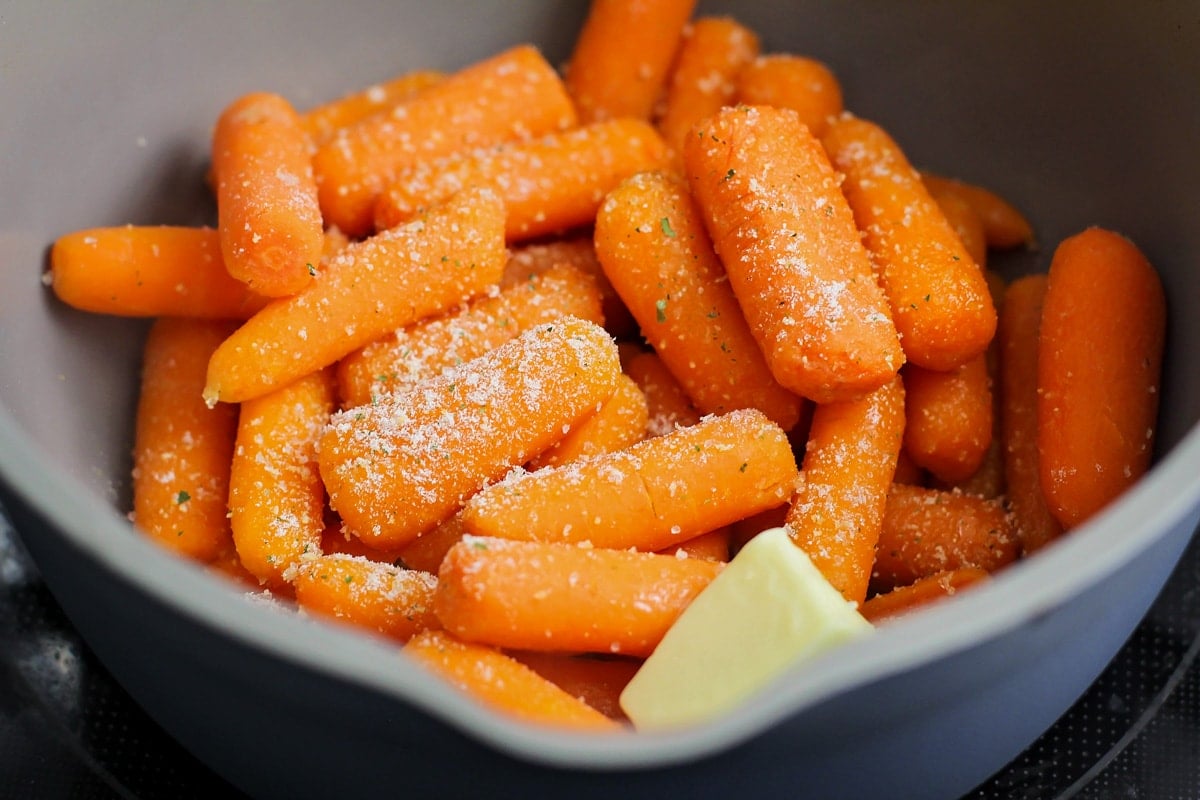 Seasoning cooked carrots in a grey bowl.
