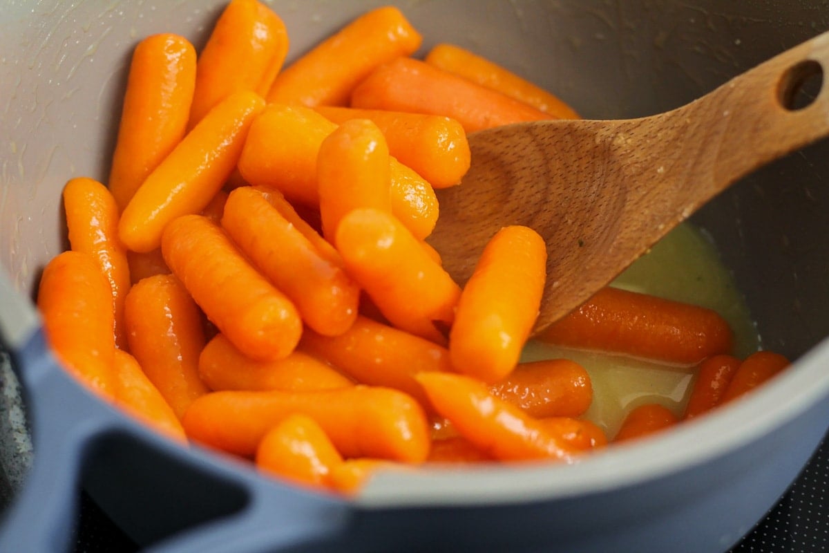 Mixing cooked carrots with butter and seasonings.