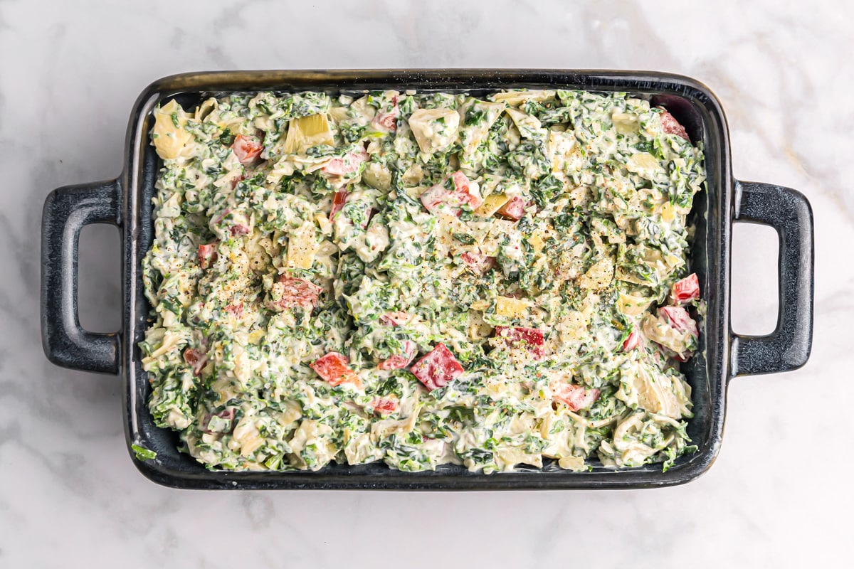 A baking dish filled with a spinach, artichoke, sour cream mixture.