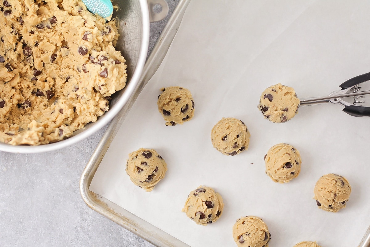 Scooping chocolate chip cookie dough onto a lined baking sheet.