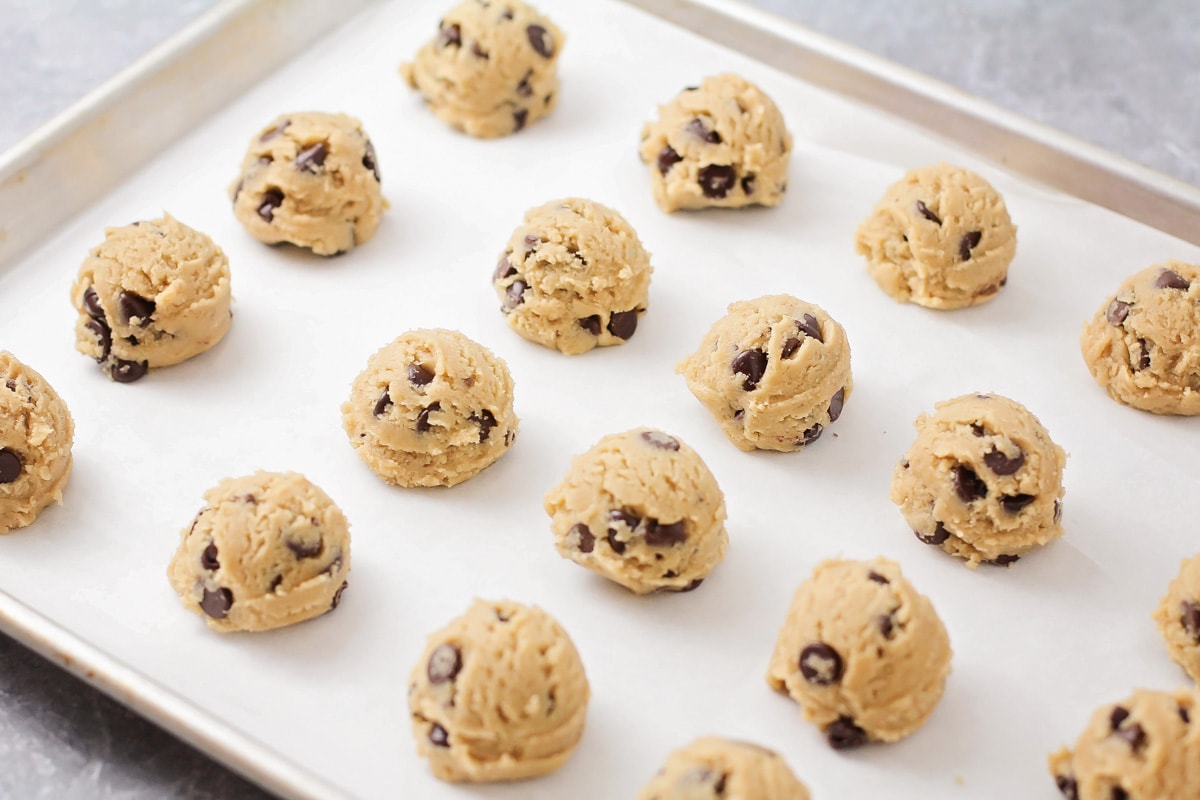 A lined sheet pan topped with chocolate chip cookie dough balls.