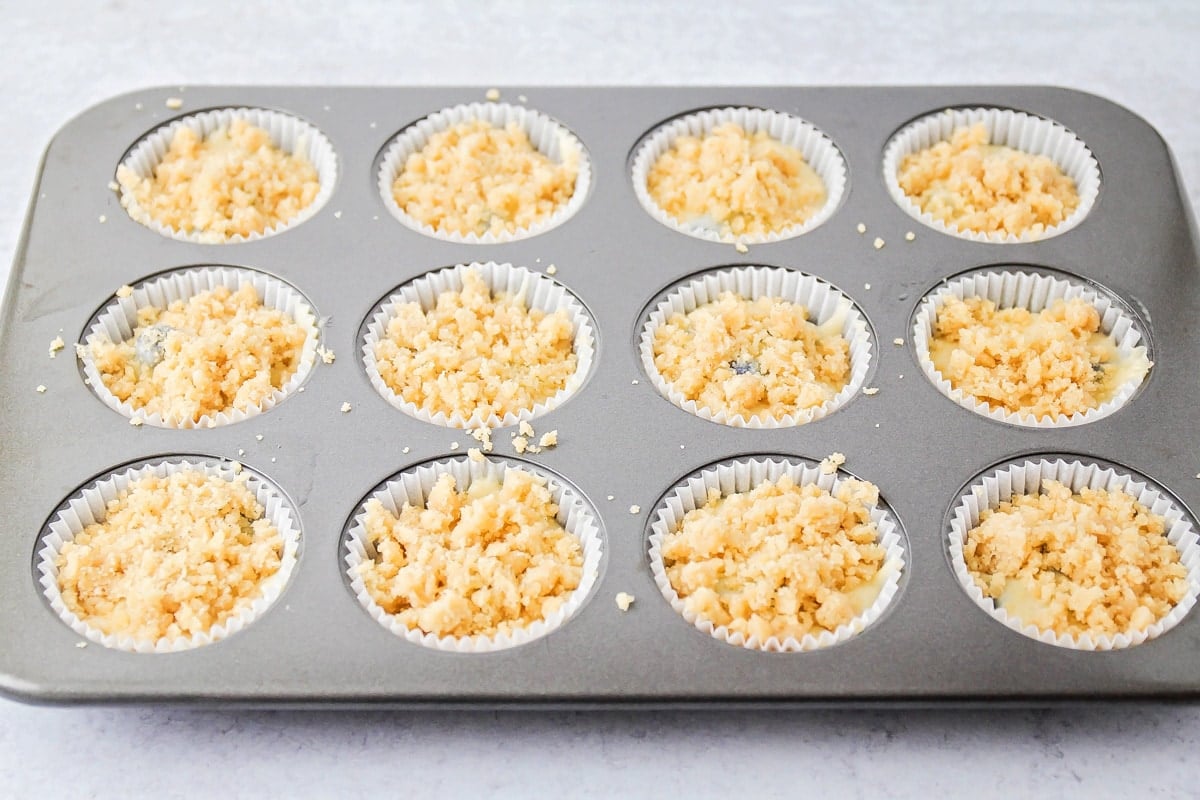 Adding streusel to the top of a blueberry muffin.