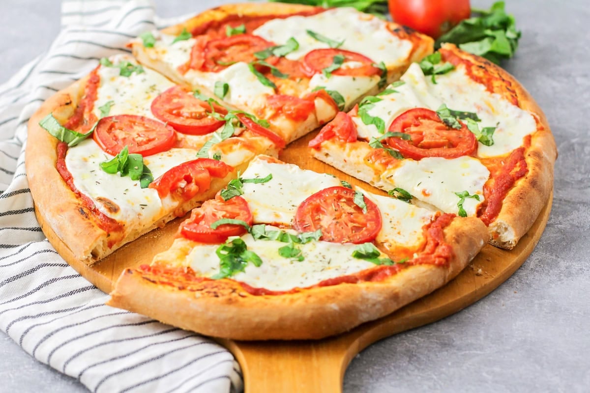 Margherita pizza stars fresh basil, mozzarella cheese, and the best ripe tomatoes. It's simple, delicious, and light. Baked margherita pizza on a pizza peel cut into quarters.