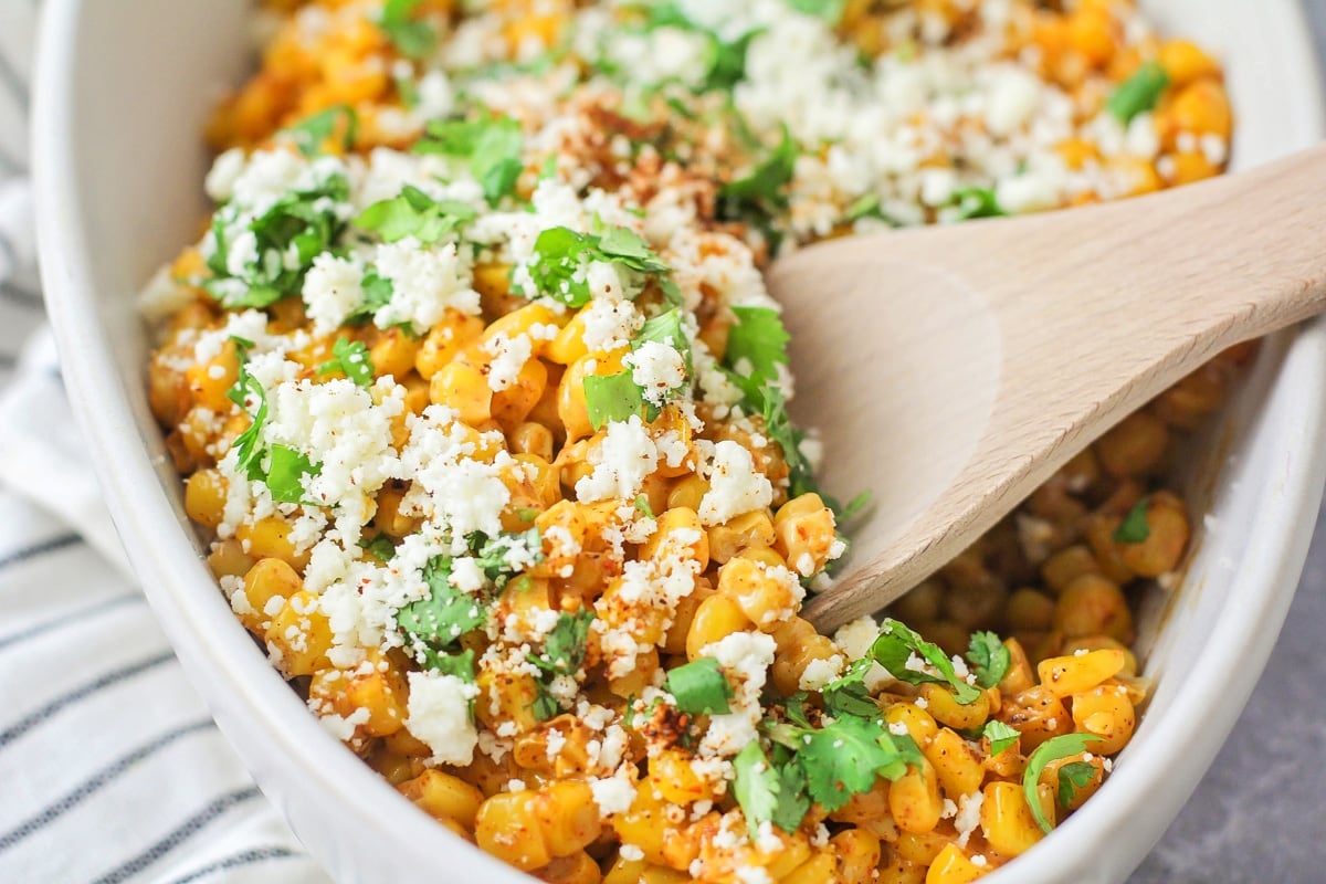 Scooping mexican street corn from a white bowl.