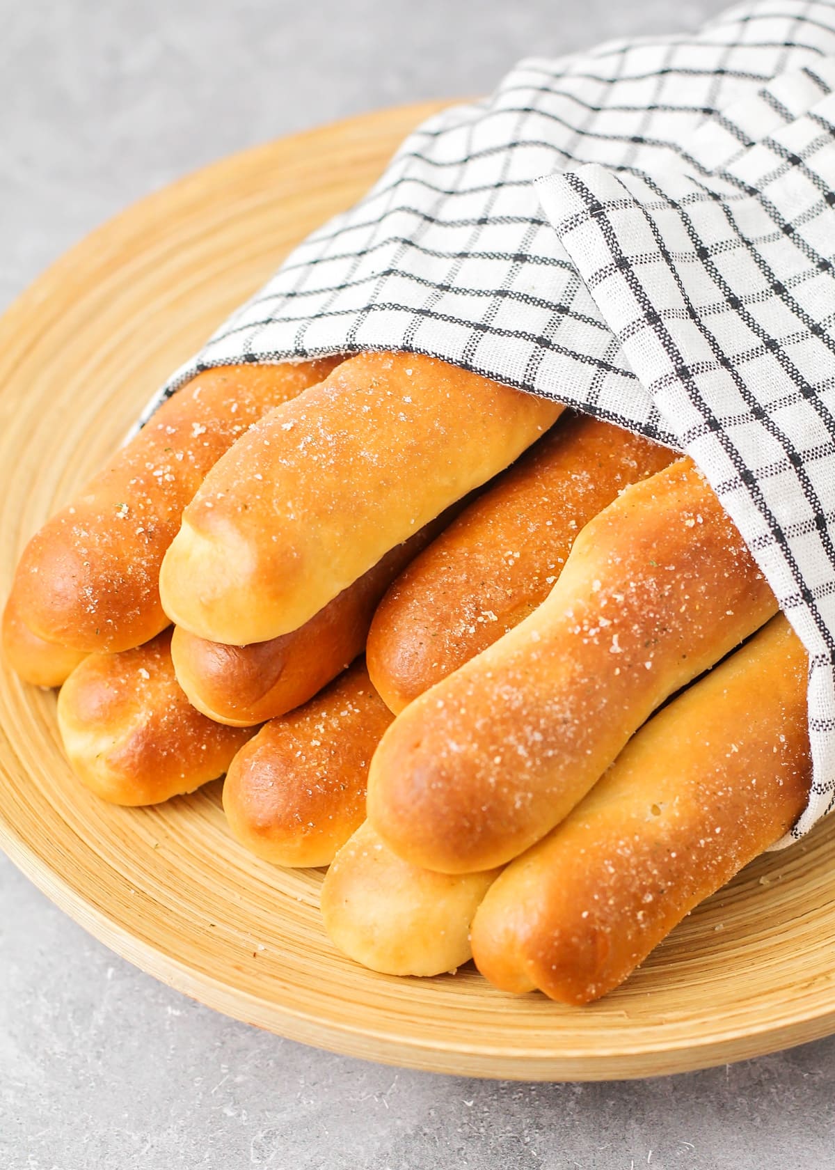 Close up of Olive Garden breadsticks wrapped in a towel on a wooden plate.
