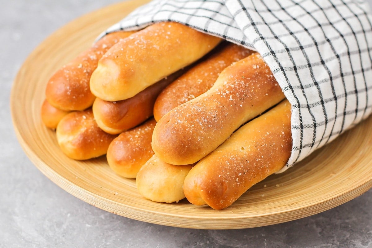 Olive Garden breadsticks wrapped in a towel on a wooden plate.