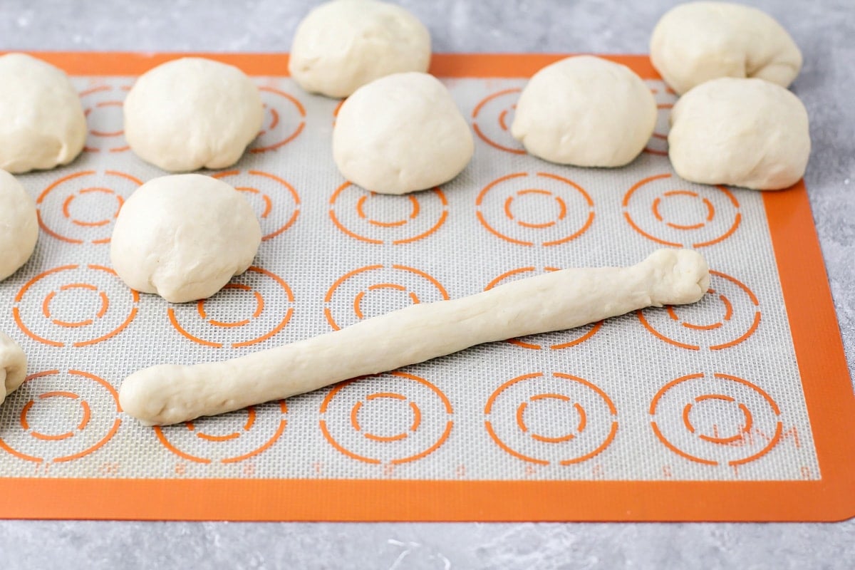 Dough balls on a mat with one rolled into a breadstick shape.