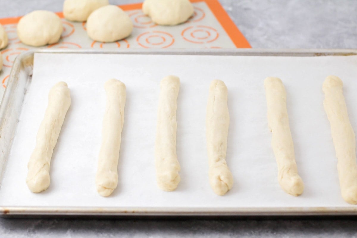 Dough rolled into breadsticks placed on a lined baking sheet.