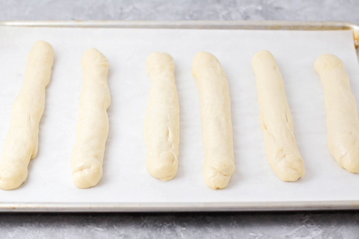 Rising breadsticks lined up on a baking sheet.