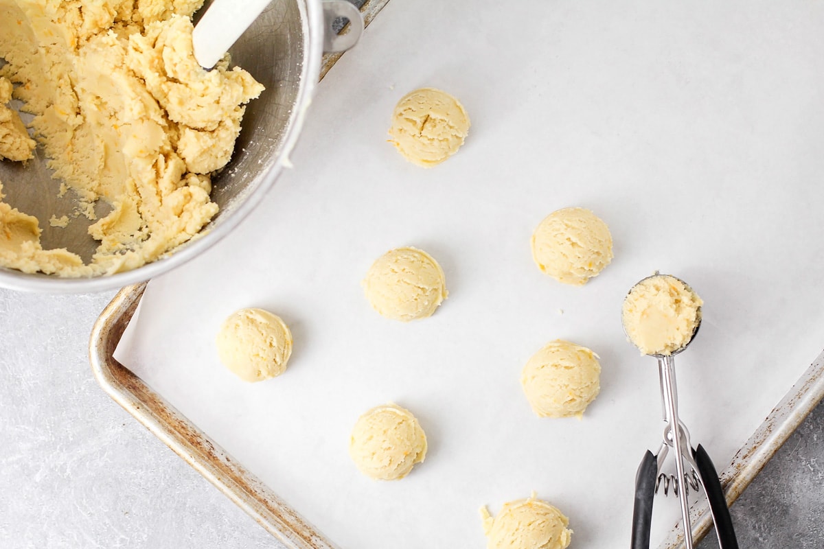 Scooping cookie dough balls onto a lined baking sheet.