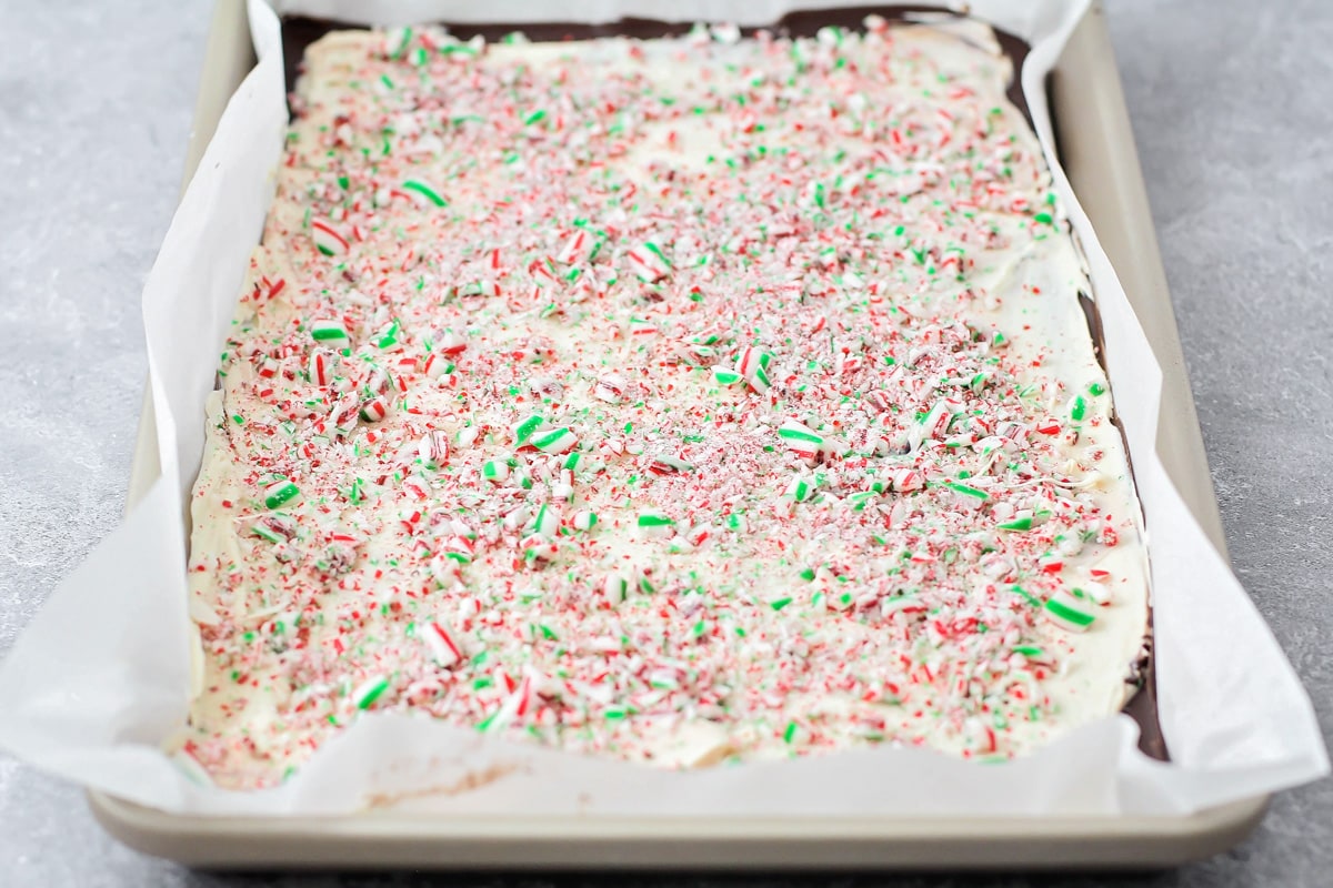Dark chocolate, white chocolate  and crushed candy canes spread on a lined baking sheet.