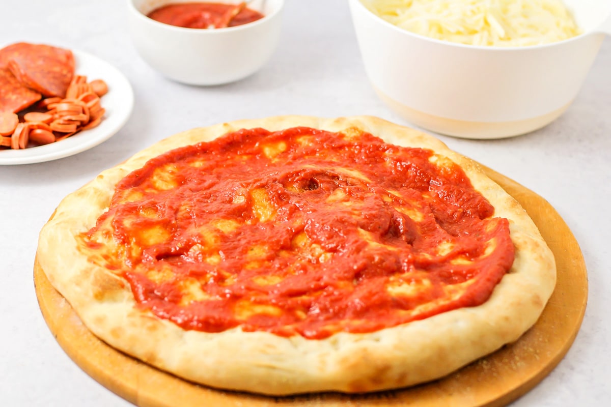 Red pizza sauce recipe spread over pizza crust.