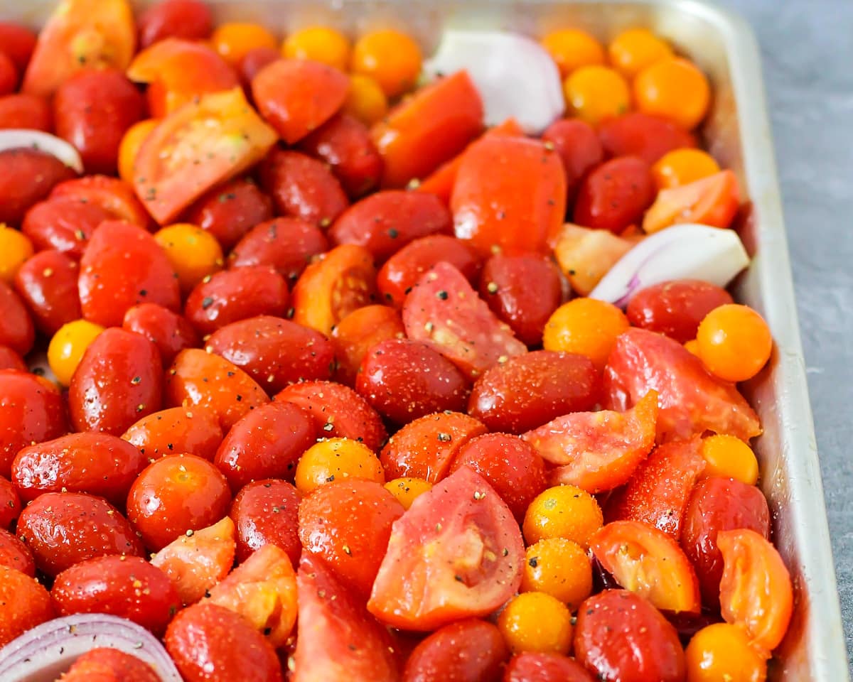 Tomatoes sliced and seasoned and spread on a baking sheet.